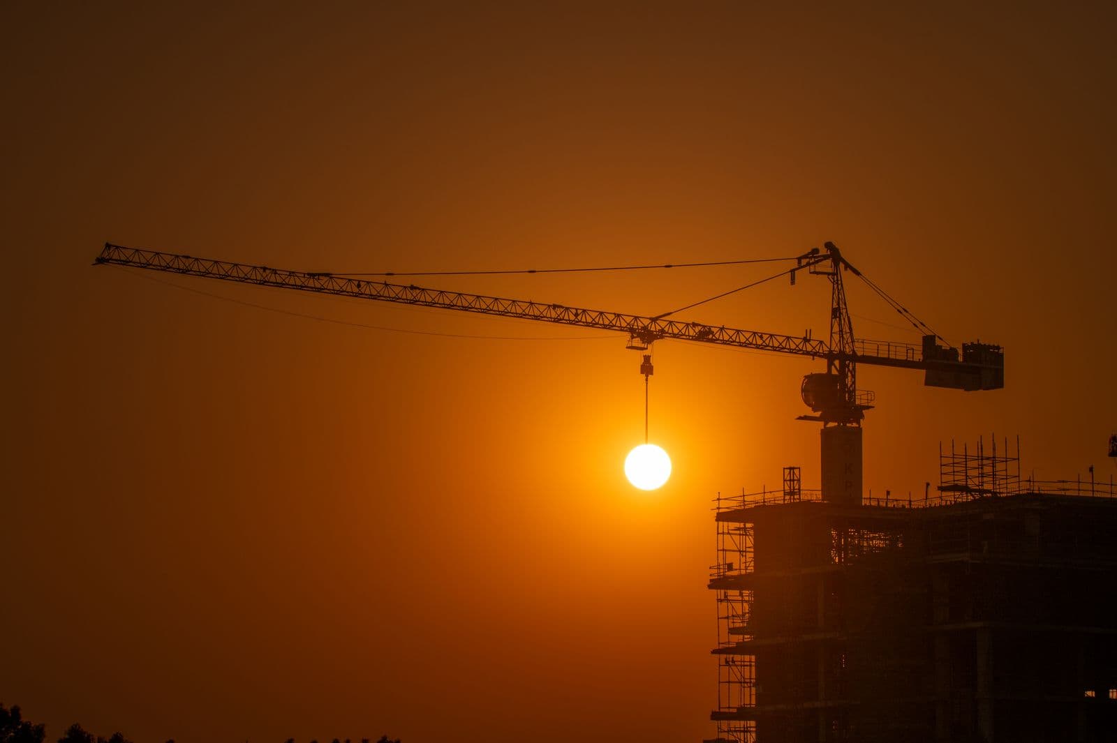 A construction crane silhouetted against the Dubai skyline at sunset